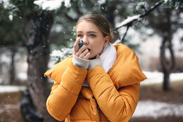 Young woman with inhaler having asthma attack outdoors