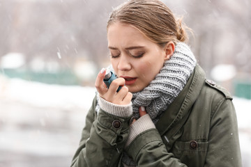 Young woman with inhaler having asthma attack outdoors
