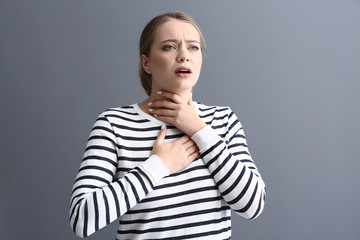 Young woman having asthma attack on grey background