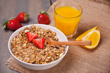 A plate with muesli, strawberries, orange juice on the wooden table