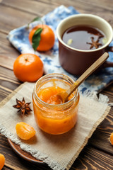 Jar of tasty tangerine jam with cup of tea on wooden table