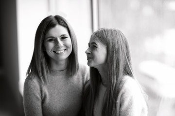 Black and white portrait of happy mother and daughter near window