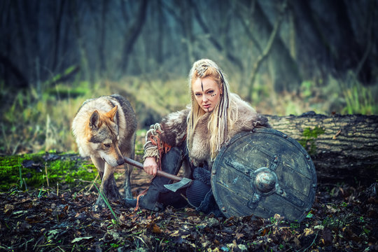 Viking warrior woman holding shield and ax  alone in woods with wolf next to her ready to attack 