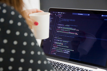 Woman programmer with cup of coffee working on laptop computer in office