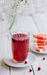 Hot fruit tea with wild berry on a white wooden table. Grapefruit slices, cranberry and cowberry. Glass cup or mug. White flowers. Berry beverage. 