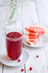 Hot fruit tea with wild berry on a white wooden table. Grapefruit slices, cranberry and cowberry. Glass cup or mug. White flowers. Berry beverage. 