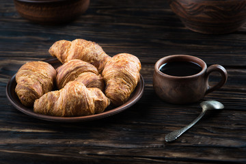 chocolate croissants are in the clay plate, next to it is a spoon and a cup of coffee
