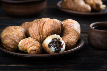 chocolate croissants are in the clay plate, next to it is a spoon and a cup of coffee