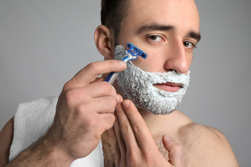 Handsome man shaving against grey background