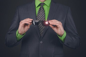 Black sunglasses in a businessman hands on a black background. Conspiracy concept.
