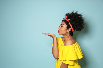 Portrait of young African-American woman blowing kiss on color background