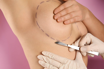 Naked woman and doctor with lancet on color background, closeup. Concept of breast augmentation