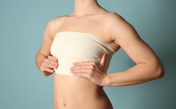Woman with bandage on her chest against color background. Breast augmentation concept