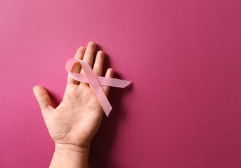 Female hand with pink ribbon on color background. Breast cancer awareness concept
