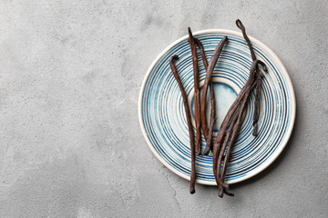 Plate with aromatic vanilla sticks on grey background