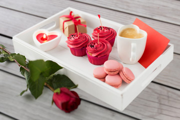 valentines day and sweets concept - close up of cupcakes with red buttercream frosting and heart shaped cocktail sticks, macarons, candle, coffee cup and gift box on tray