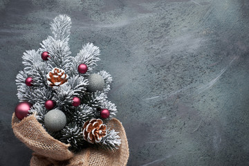 Small Christmas tree in sackcloth decorated with red baubles and berries on dark textured background