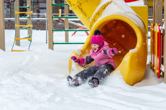 Little cute baby girl having fun on playground at winter. Children winter sport and leisure outdoor activities