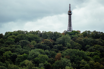 The Petřín Lookout Tower, steel metal framework almost replica of the Eiffel Tower, in Prague, Czech Republic - seen through a forest of trees from Prague Castle on a cloudy day