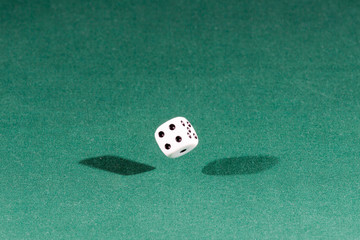 One white dice falling on a green table