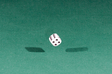 One white dice falling on a green table
