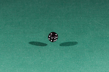 One black dice falling on a green table