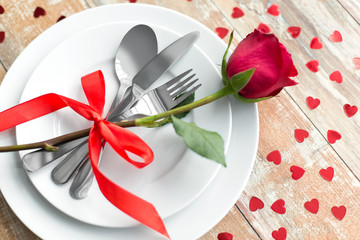 valentines day, table setting and romantic dinner concept - close up of red rose flower on set of dishes with cutlery on wooden background