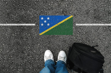 a man with a shoes and backpack is standing on asphalt next to flag of Solomon Islands and border