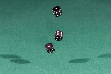 Three black dices falling on a green table