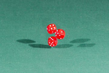 Three red dices falling on a green table