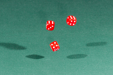 Three red dices falling on a green table
