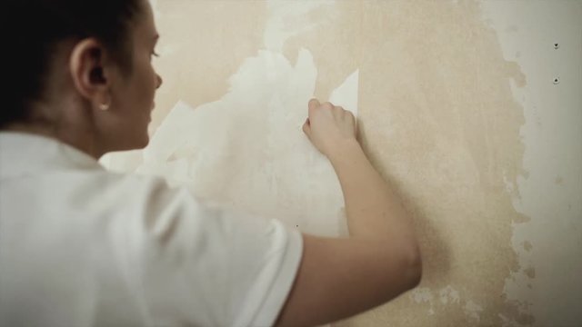 Woman hand scrapes wallpaper off walls. Removing the wallpaper in the room. Girl tears off wallpaper