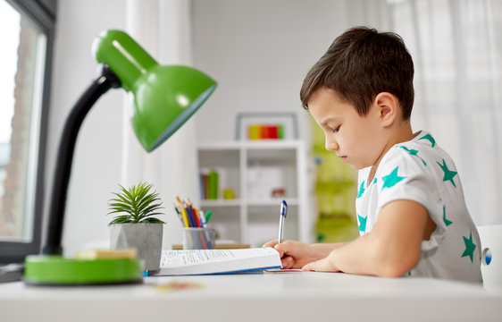 education, childhood and school concept - student boy with book writing to notebook at home