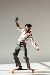 handsome bearded man riding longboard on grey background