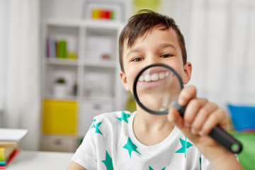 childhood, fun and curiosity concept - happy little boy with magnifier showing big teeth at home