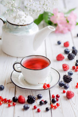 Berry red tea on a white wooden table. White porcelain cup, teapot with tea. 