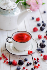 Berry red tea with fresh raspberries, currant, strawberries, blackberries and blueberries on a white wooden table. 