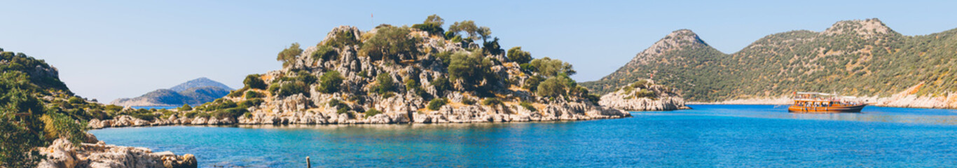 Fototapeta na wymiar Panorama view of Tourist cruise near small rocky island in Ufakdere, Kas, Antalya, Mediterranean coast of Turkey