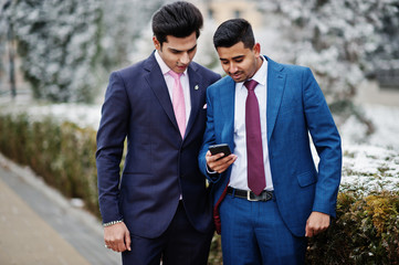 Two elegant indian fashionable mans model on suit posed at winter day looking at phone.