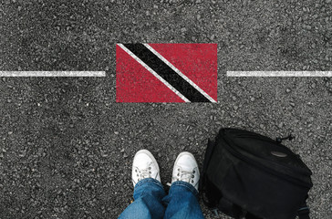 a man with a shoes and backpack is standing on asphalt next to flag of Trinidad and Tobago and...
