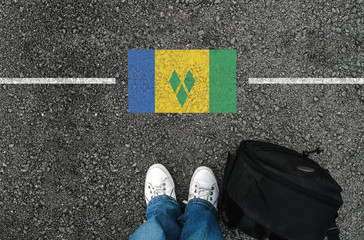 a man with a shoes and backpack is standing on asphalt next to flag of Saint Vincent and the...