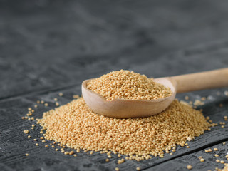 A spoon of light wood with amaranth seeds on a dakr wooden rustic table.