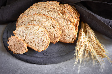 Slliced white round bread with wheat ears on wooden cutting board on gray stone