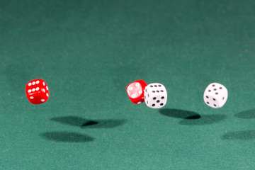 Four red and white dices falling on a green table