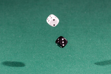 Two white and black dices falling on a green table