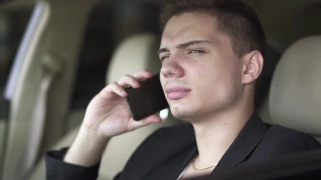Portrait of young man chewing gum and talking by cell phone in the car close up