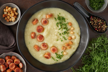 Flat lay of homemade cream of potato soup with croutons, fried vienna sausages and green coriander