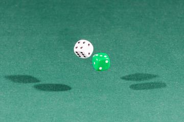 Two white and green dices falling on a green table