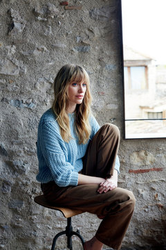 Junge Frau sitzt leger auf Hocker auf einer Dach Terrasse  vor Steinwand mit Blick auf Altstadt