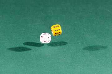 Two white and yellow dices falling on a green table